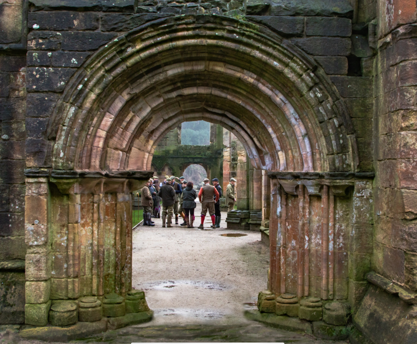 Guests gathering for mid-morning drinks beneath a stone arch at Fountains Abbey